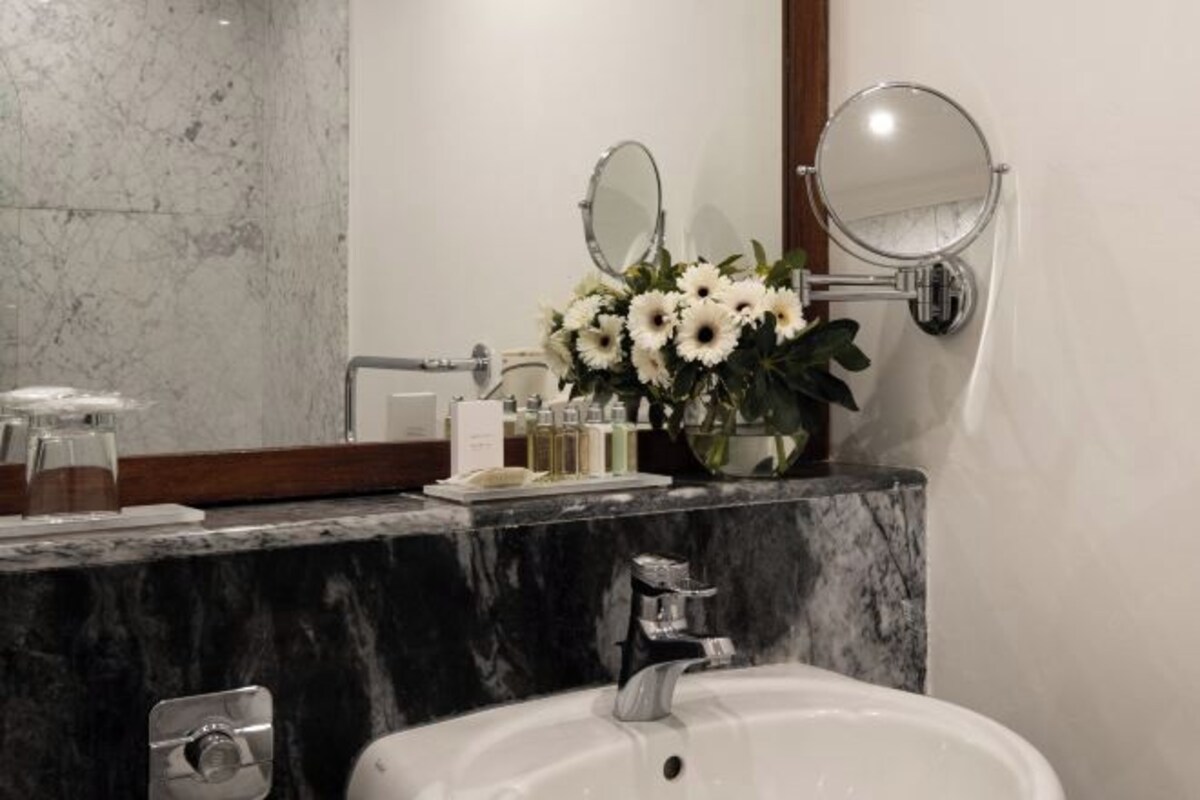 Un baño con lavamanos de mármol, dos espejos y un florero con flores.