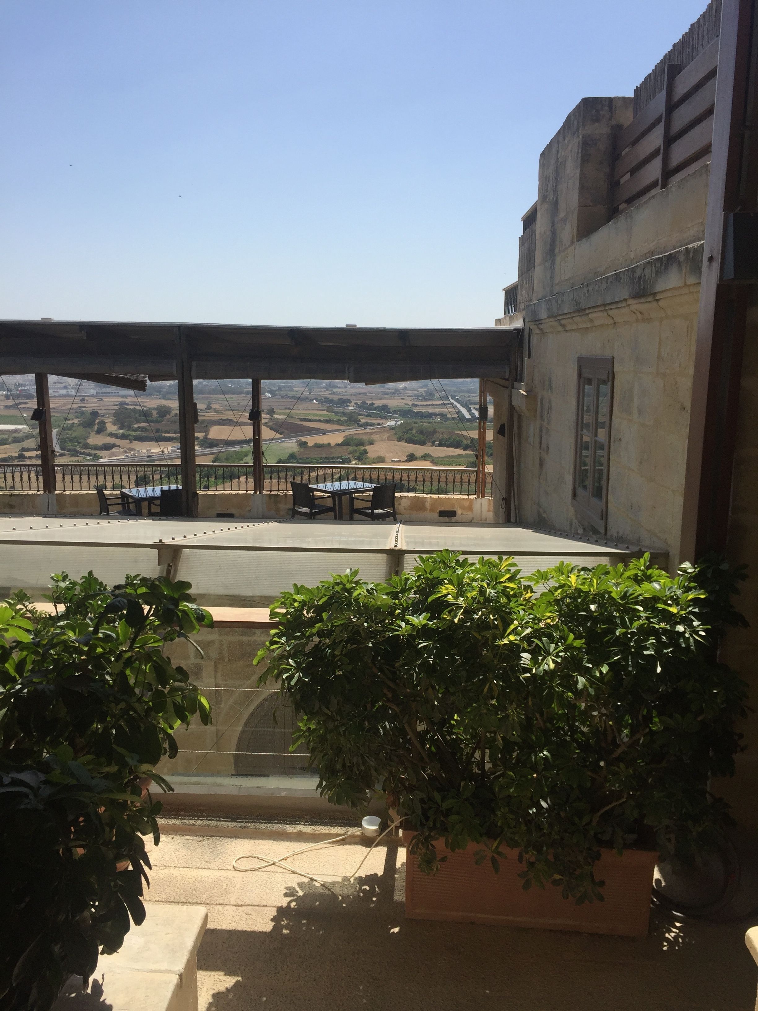 A terrace with a view of the countryside, a table, chairs, and potted plants.