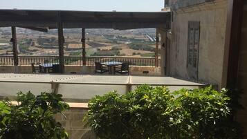 A terrace with a view of the countryside, a table, chairs, and potted plants.