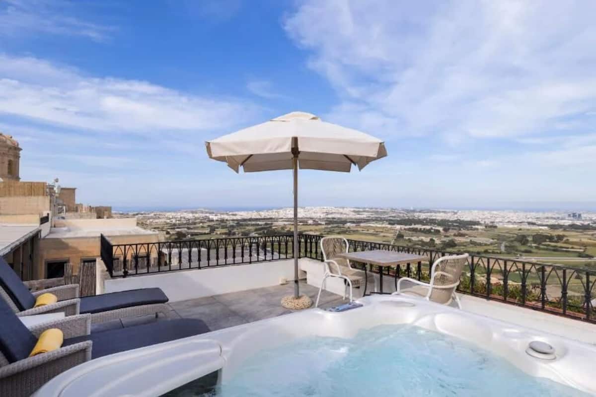 Terraço no telhado com hidromassagem, espreguiçadeiras e um guarda-sol.