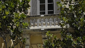 A building facade with a central entrance, flanked by potted plants and a decorative balustrade.