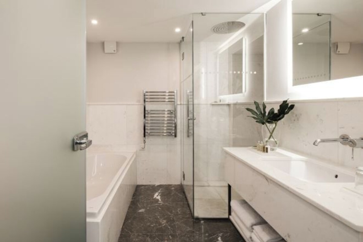 Un baño moderno con cabina de ducha de vidrio, una bañera blanca y un lavabo con espejo.