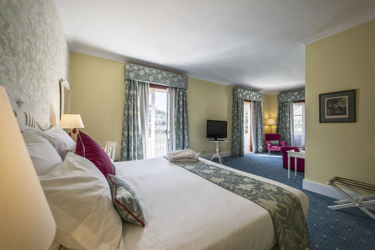 Habitación de hotel con una cama grande, un escritorio, una silla, un televisor y una ventana con cortinas.
