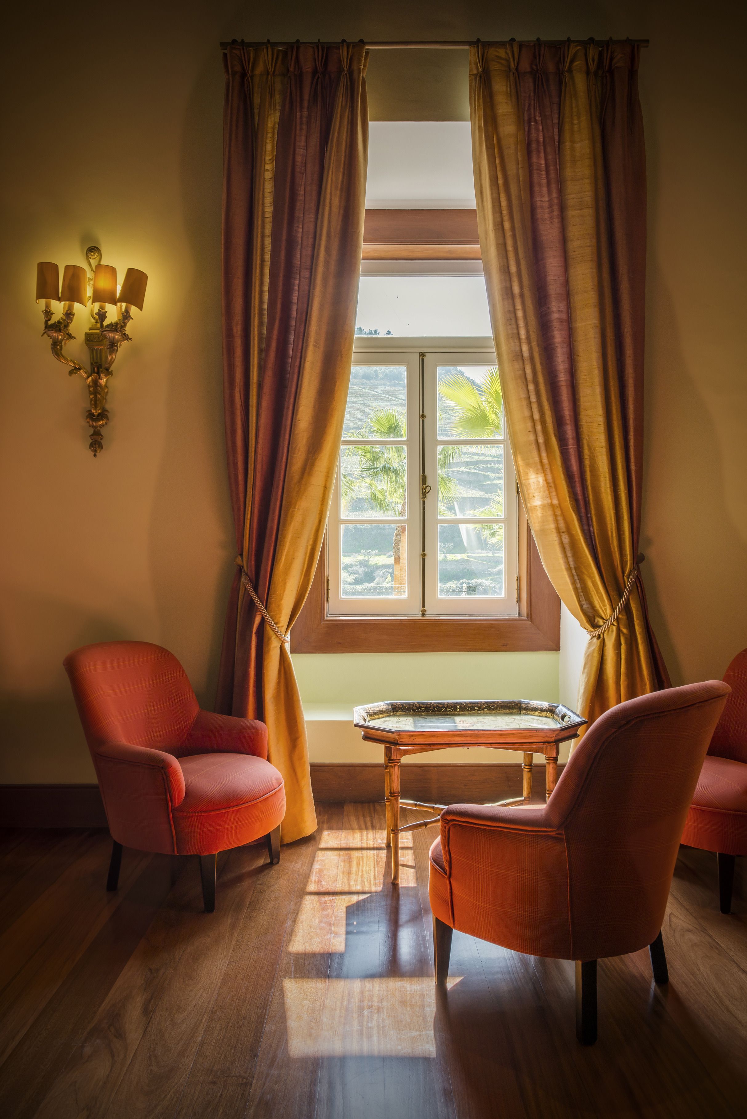 Ein Zimmer mit zwei roten Stühlen, einem kleinen Tisch und einem Fenster mit Vorhängen.