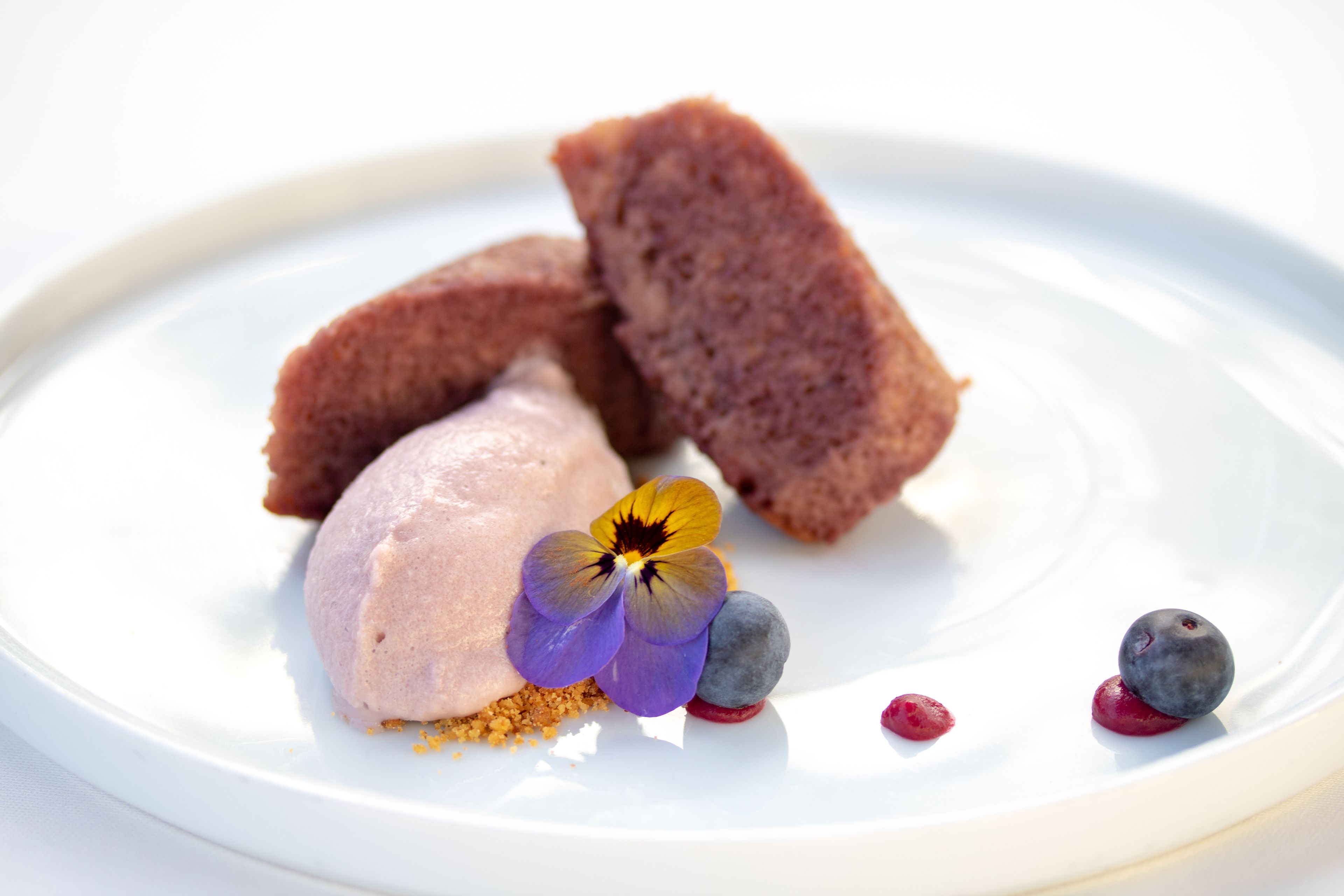Un plato de postre con helado, bayas y una flor.