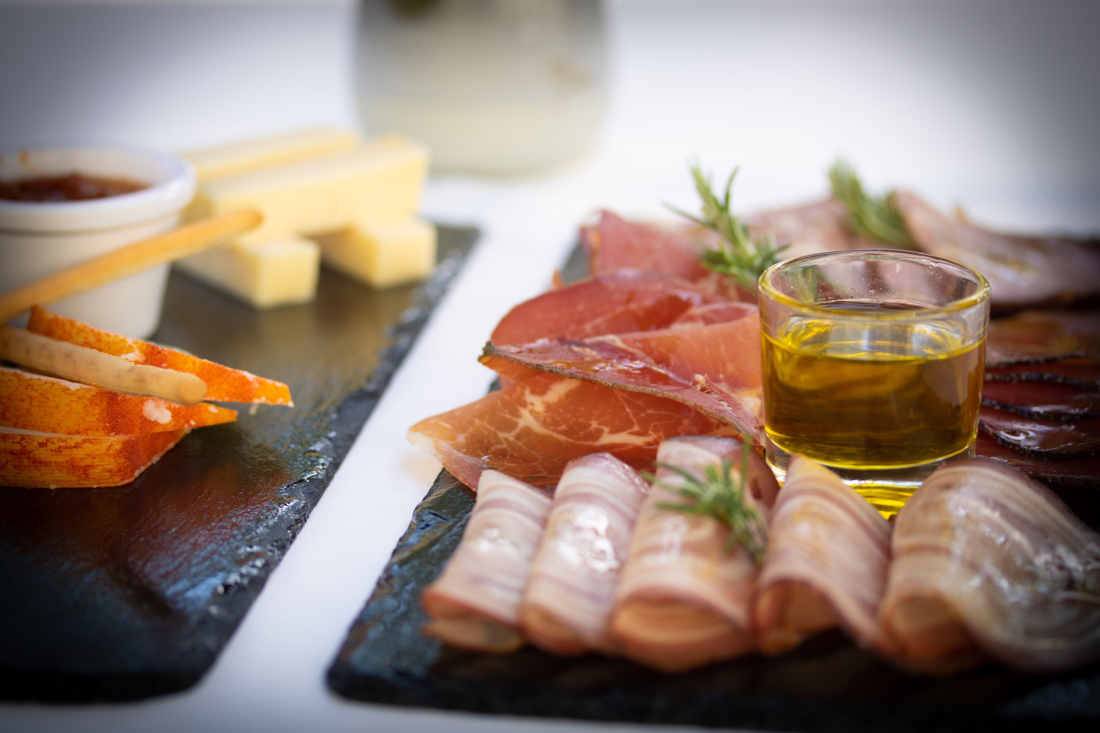A charcuterie board with various meats, cheese, and a glass of oil.
