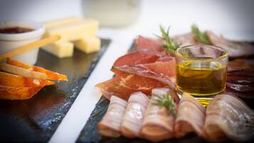 A charcuterie board with various meats, cheese, and a glass of oil.