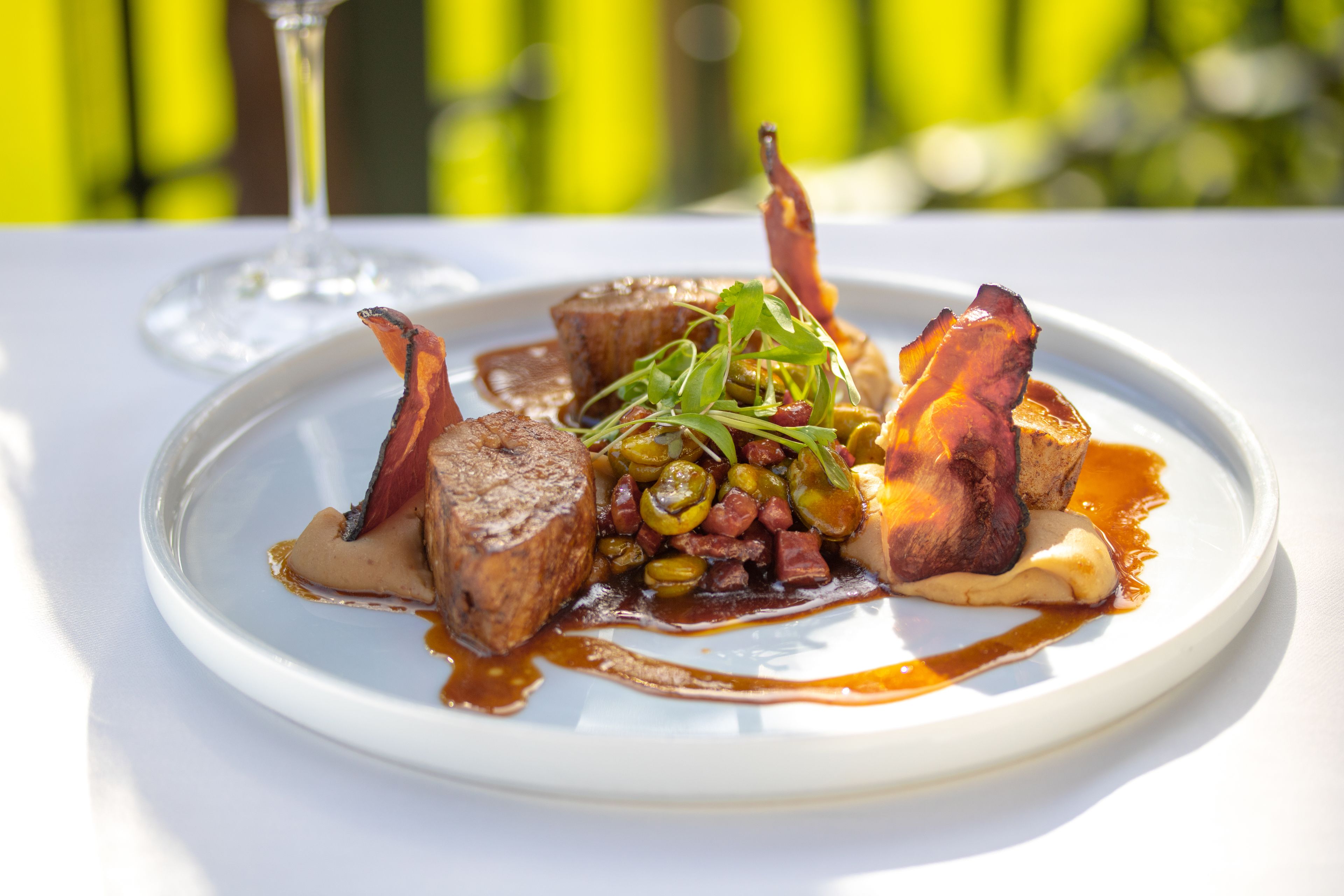 A plate of food with various meats and vegetables, a glass of wine, and a white tablecloth.