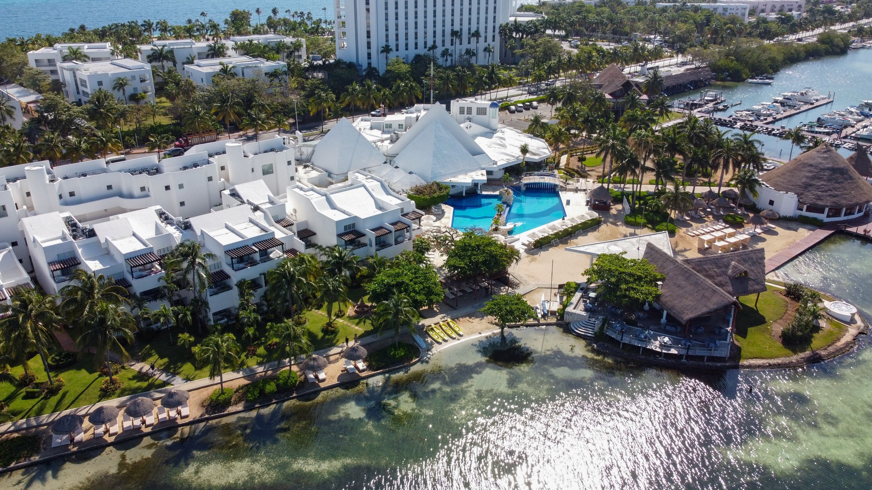 Un resort con varias edificaciones blancas, una piscina central y un puerto deportivo.
