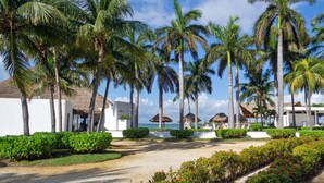 Ein Resort mit Palmen, Strand und strohgedeckten Gebäuden.