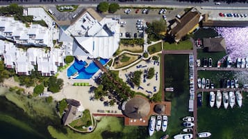 Vista aèria d'un complex turístic amb una piscina, un port esportiu amb vaixells i una zona d'aparcament.
