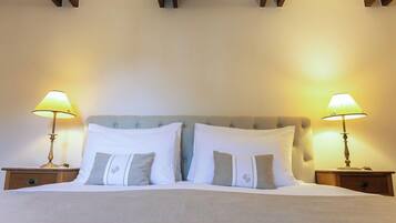 A neatly made bed with white and gray pillows, flanked by two bedside tables with lamps, in a room with wooden beams on the ceiling.