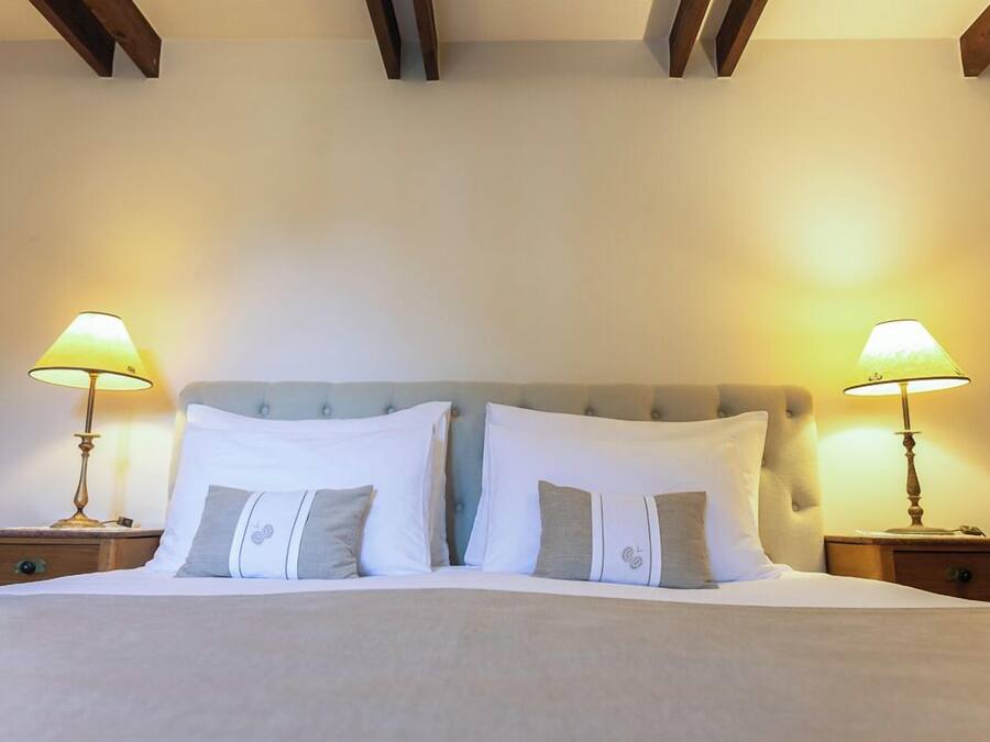 A neatly made bed with white and gray pillows, flanked by two bedside tables with lamps, in a room with wooden beams on the ceiling.