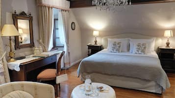 A bedroom with a large bed, two bedside tables with lamps, a desk with a chair, a round table with a vase, and a chandelier.