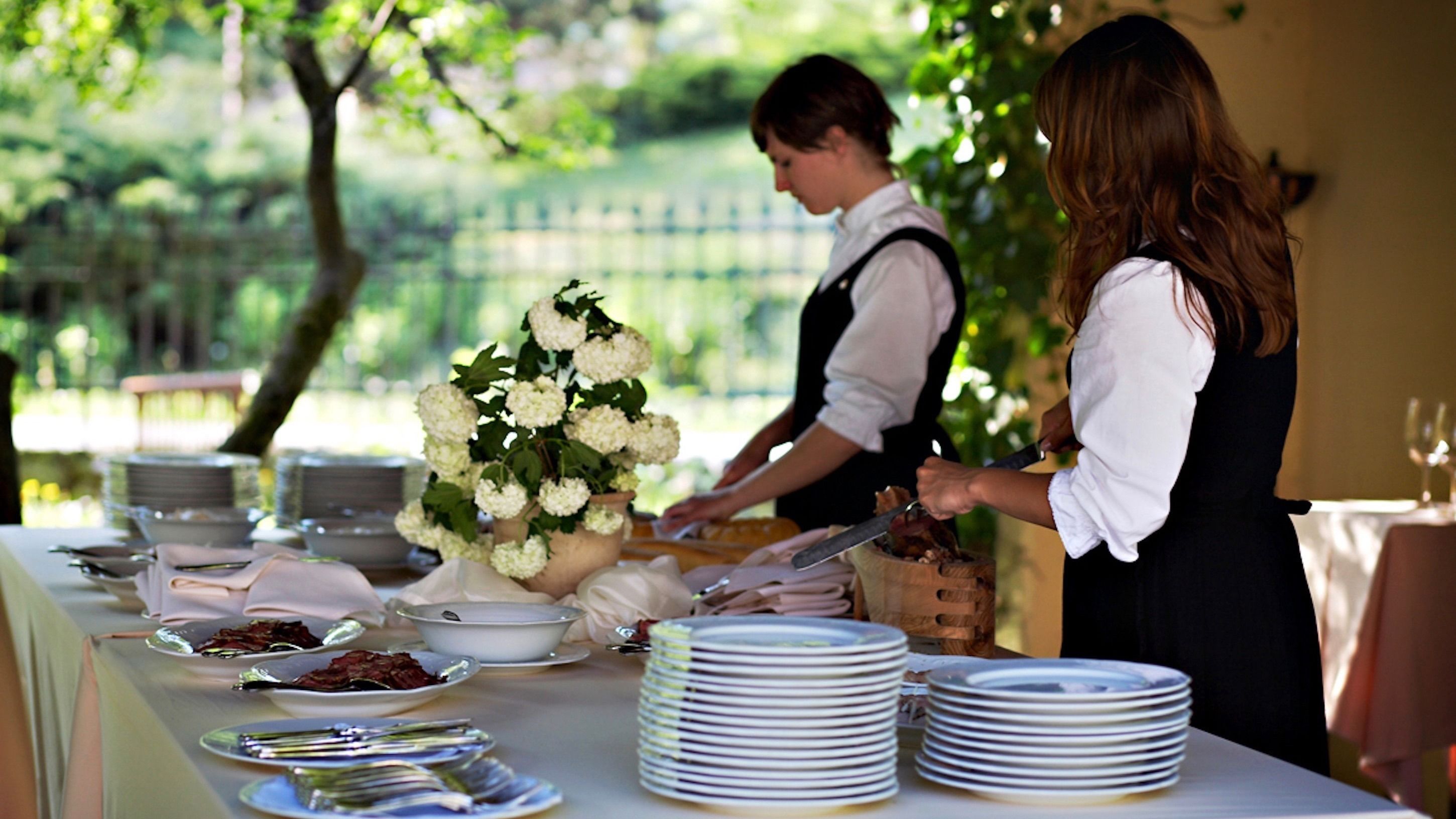 Montaje de bufé con platos blancos, cubiertos y un centro de mesa con flores blancas.