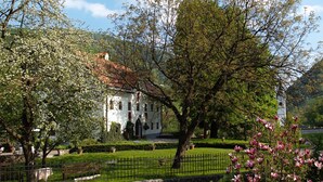 A white building with a red roof, surrounded by well-maintained gardens and trees. - Hotel Kendov Dvorec (Idrija)