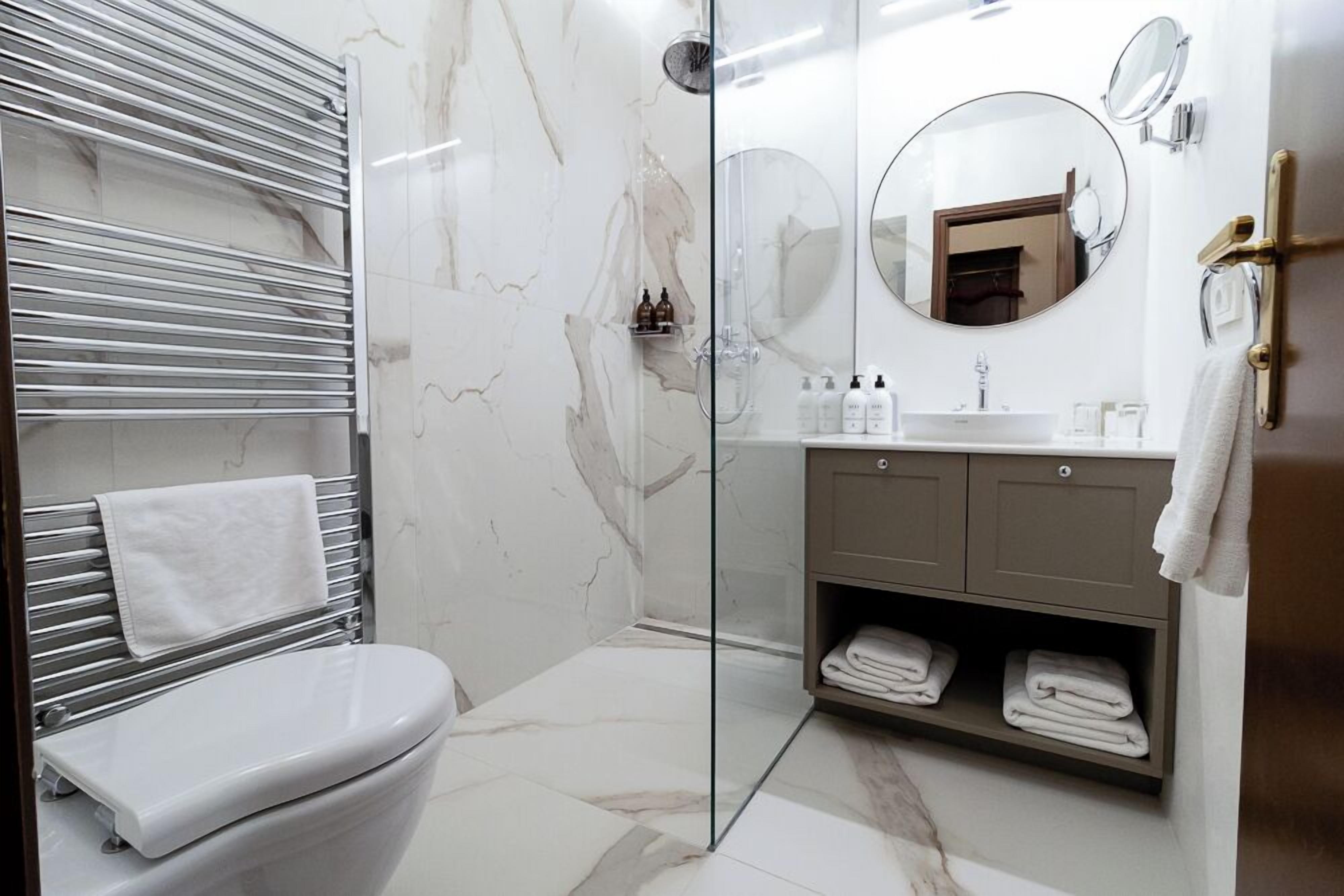 A modern bathroom with a glass-enclosed shower, a white toilet, a marble-tiled floor, a vanity with a mirror, and a towel rack.