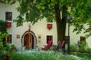 Ein Gebäude mit einem großen Baum davor, einem roten Banner mit der Nummer 1377 und einem Stuhl unter dem Baum.