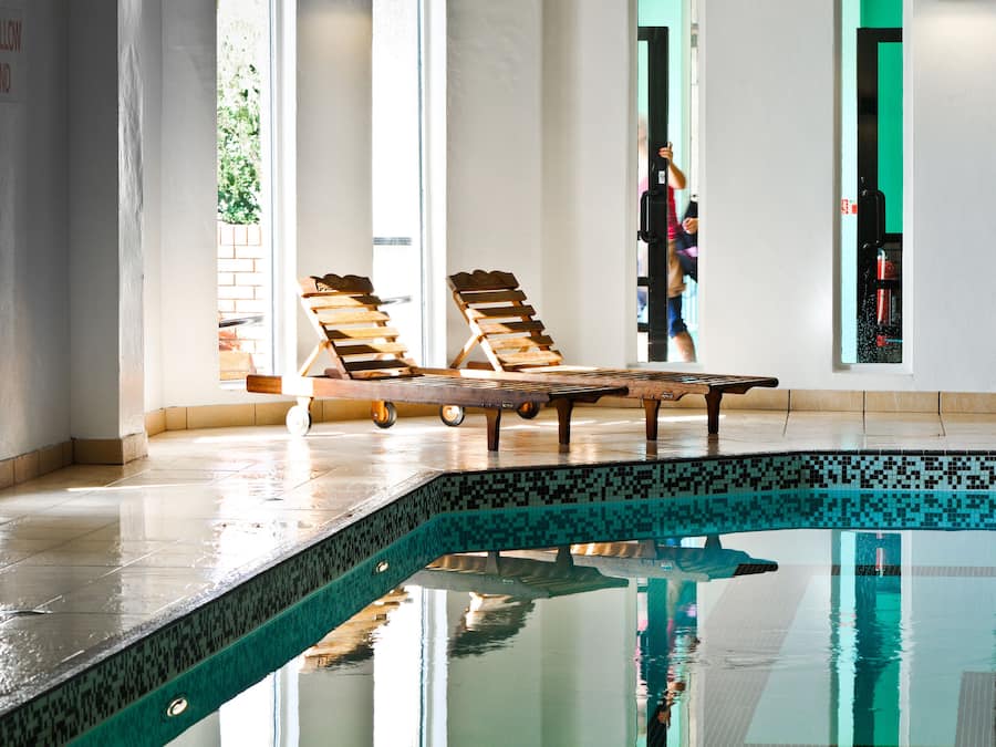 A swimming pool with two wooden loungers and a tiled deck.