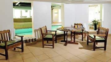 A dining area with wooden chairs and a round table, a tiled floor, and a view of an outdoor swimming pool.