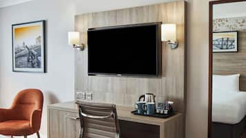 A hotel room with a wooden desk, a television, a coffee maker, and a bed.