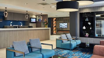 A hotel lobby with a reception desk, seating area, and a television screen.