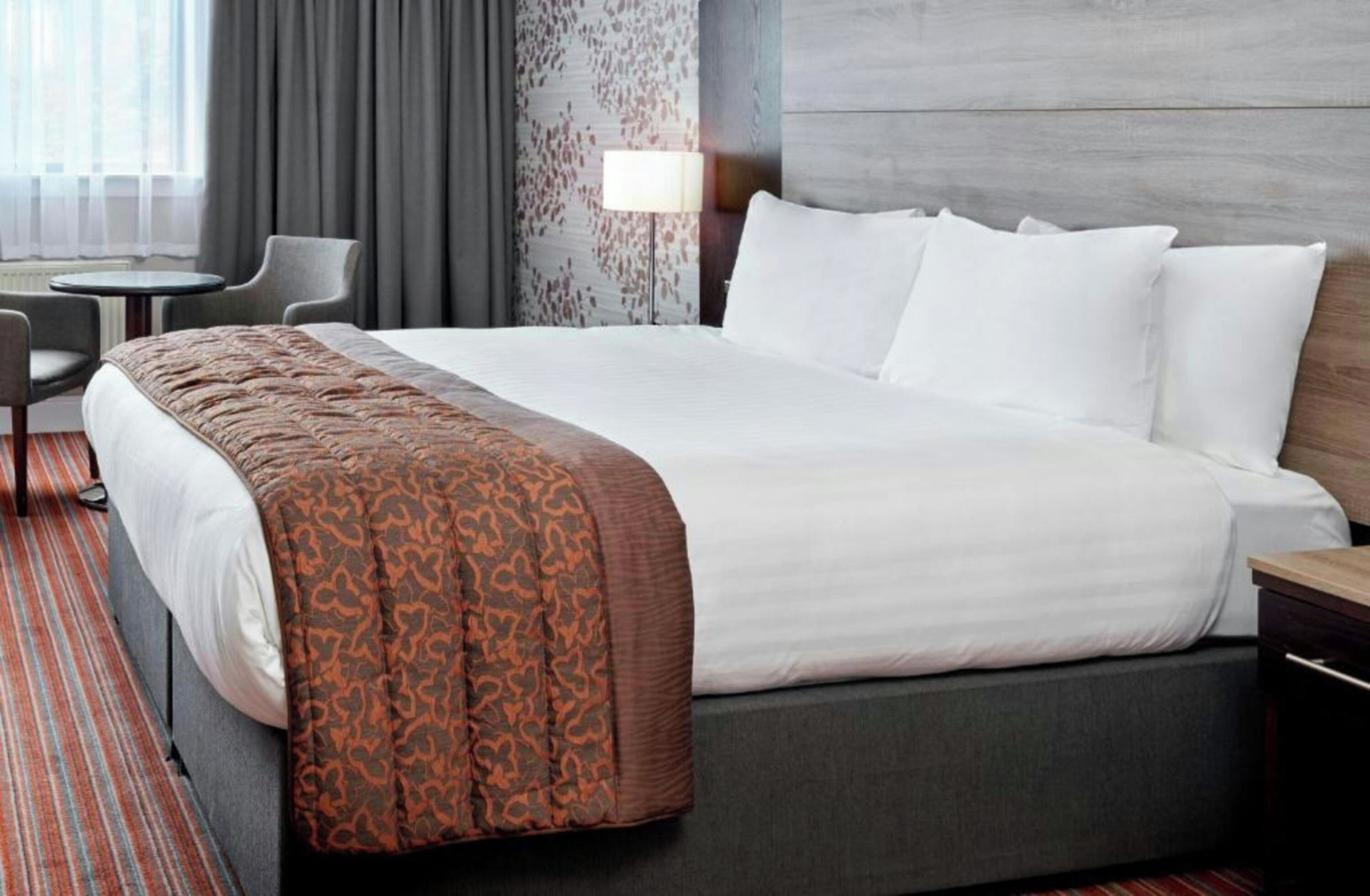 Una habitación de hotel con una cama, un escritorio, una silla y una lámpara.