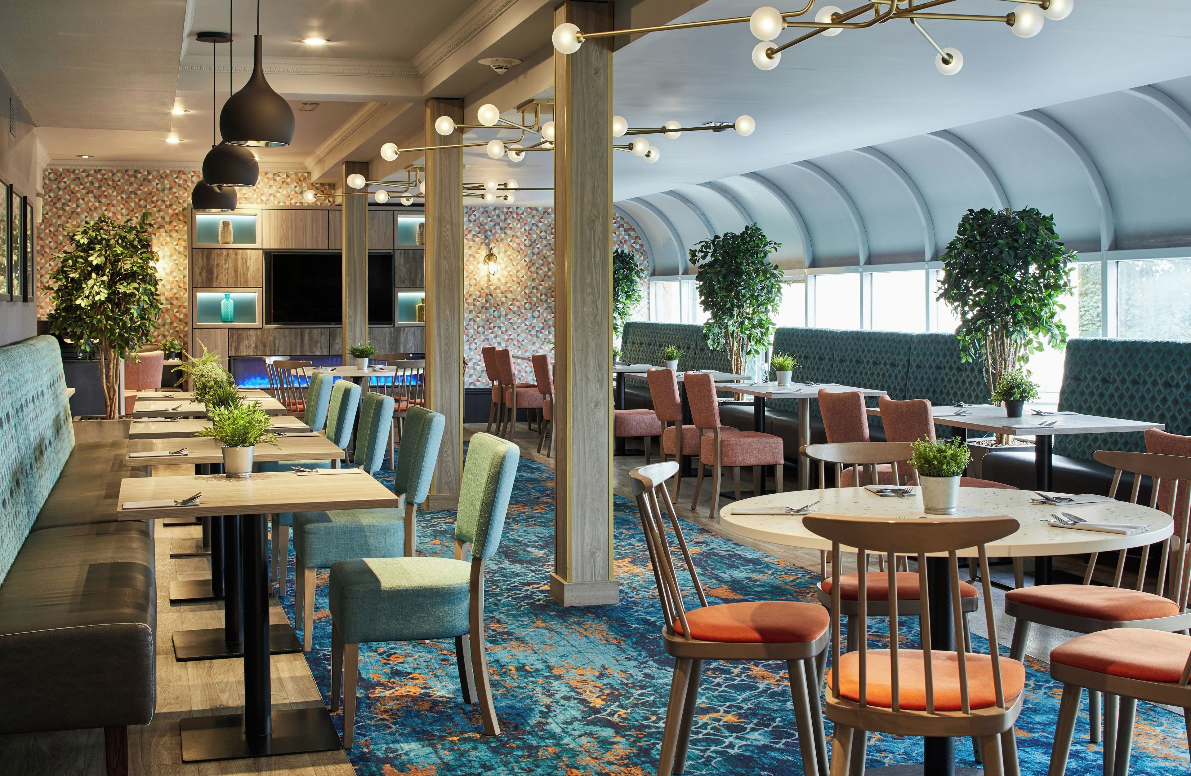 Ein modernes Restaurant mit verschiedenen Sitzbereichen, darunter gemütliche Nischen und runde Tische, und einer vielfältigen Bepflanzung.