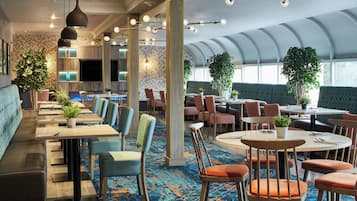 Un restaurante moderno con varias zonas de estar, incluyendo cabinas y mesas redondas, y una variedad de plantas.