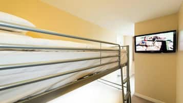 A bunk bed with metal railings, a television mounted on the wall, and a beige wall.