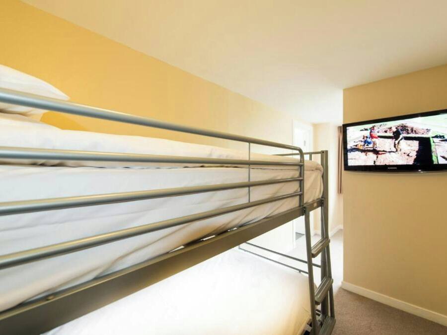A bunk bed with metal railings, a television mounted on the wall, and a beige wall.