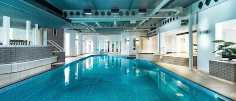 An indoor swimming pool with clear blue water, surrounded by a modern architectural design with white walls and a blue ceiling.