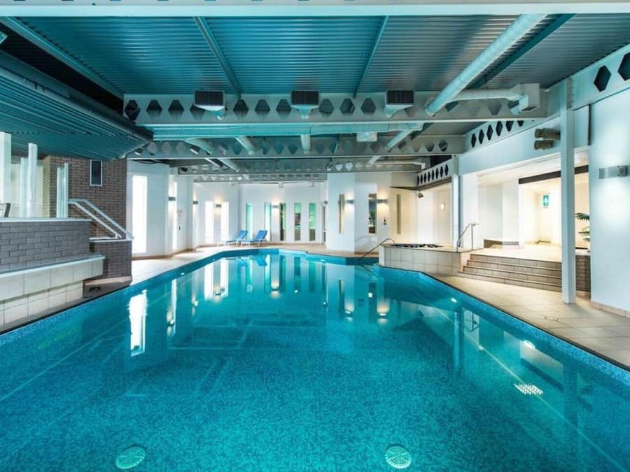 Una piscina interior con agua azul cristalina, rodeada por un diseño arquitectónico moderno con paredes blancas y techo azul.