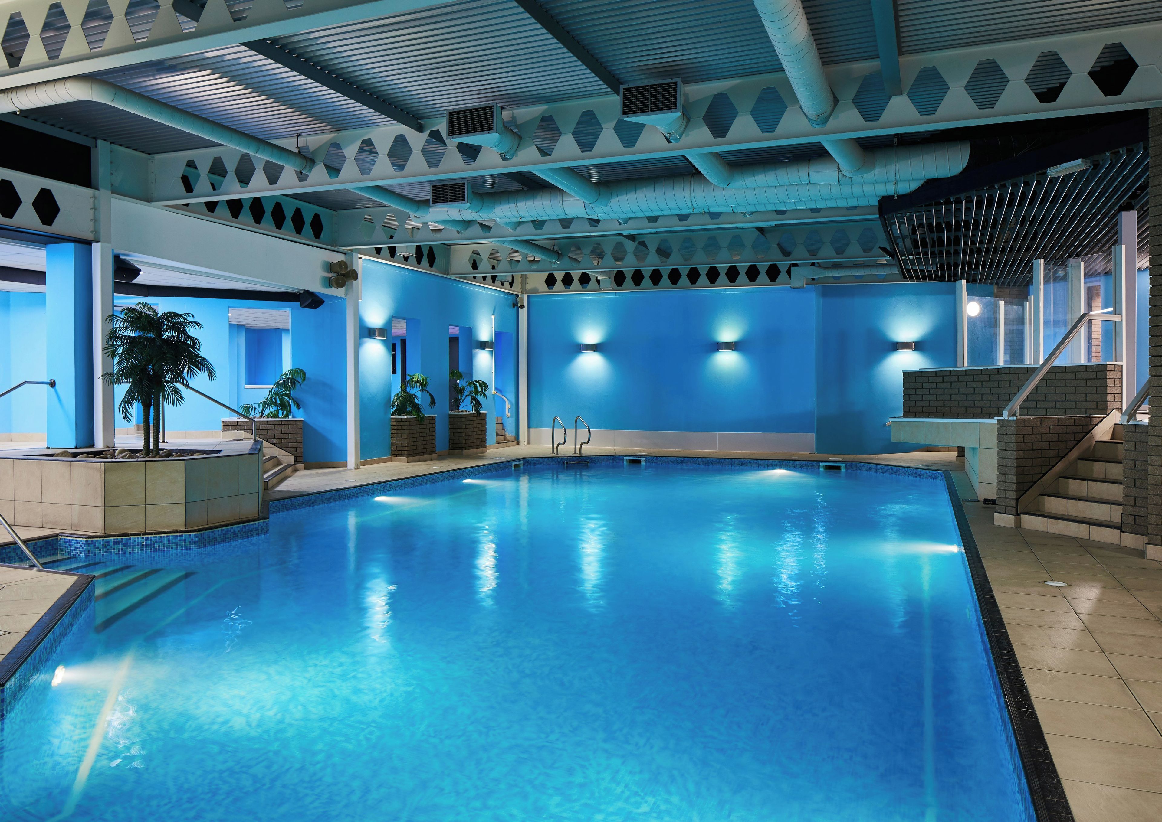 Une piscine intérieure à l’eau d’un bleu cristallin, entourée de murs ornés de motifs géométriques et dotée d’un éclairage intégré.