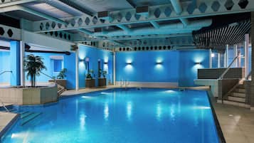 An indoor swimming pool with clear blue water, surrounded by walls with geometric patterns and built-in lighting.