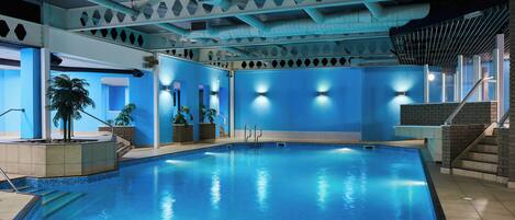 Une piscine intérieure à l’eau d’un bleu cristallin, entourée de murs ornés de motifs géométriques et dotée d’un éclairage intégré.