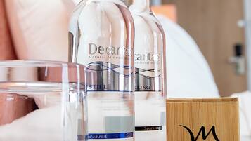 Two bottles of Decanter Mineral Water, a glass, and a wooden box with a monogram on a table in a hotel room.