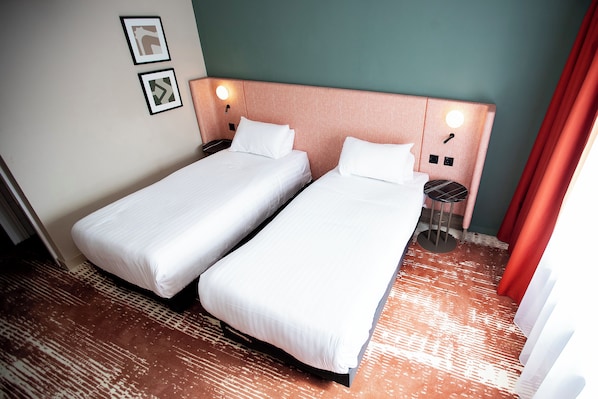 Une chambre d’hôtel avec deux lits simples, une table de chevet avec une lampe et un téléphone fixé au mur.
