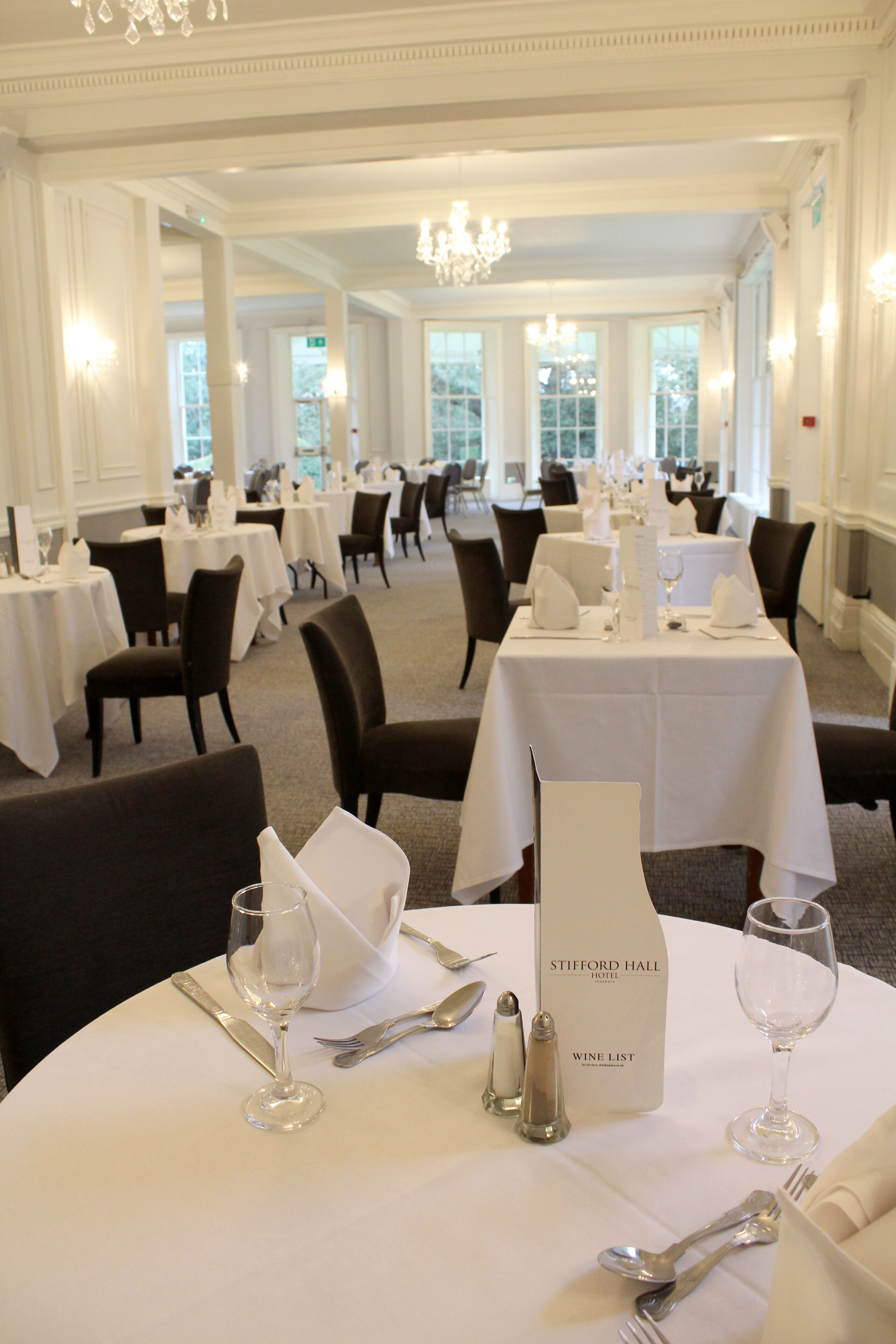 A formal dining area with multiple tables set for service, each with white tablecloths, silverware, and wine glasses.
