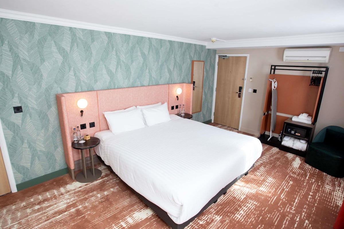 Una habitación de hotel con una cama grande, dos mesitas de noche, un espejo, un armario y un equipo de aire acondicionado.