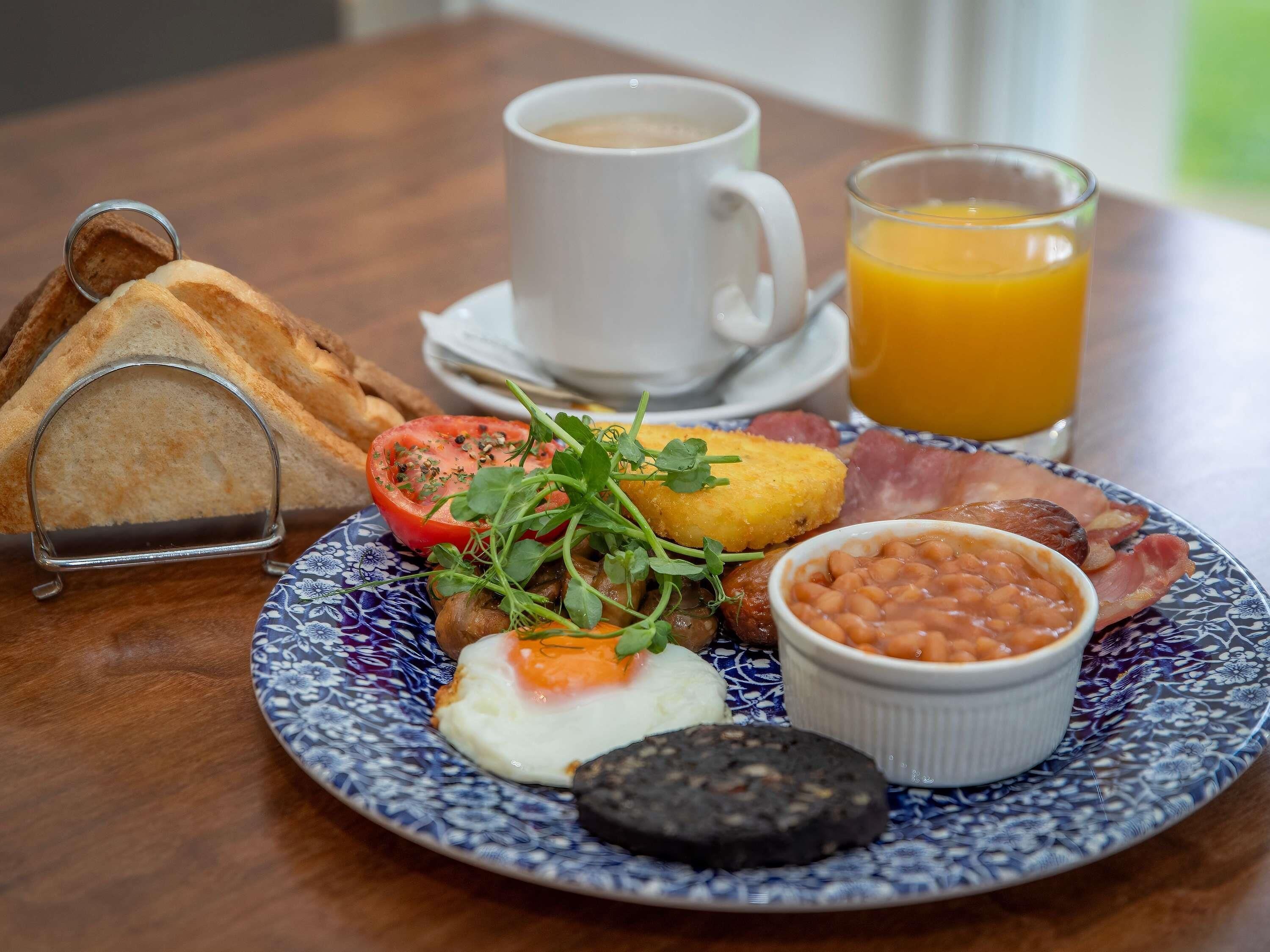 A breakfast plate with toast, eggs, beans, bacon, and a slice of black pudding, accompanied by a cup of coffee and a glass of orange juice.