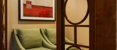 Un sofá verde con un cuadro abstracto enmarcado encima, una mesa de madera y una puerta de madera con un ventanal circular.