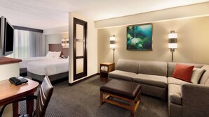 A hotel room with a bed, a sofa, a desk with a phone, and two wall-mounted lamps. - Hyatt Place Baltimore/Owings Mills (Owings Mills)