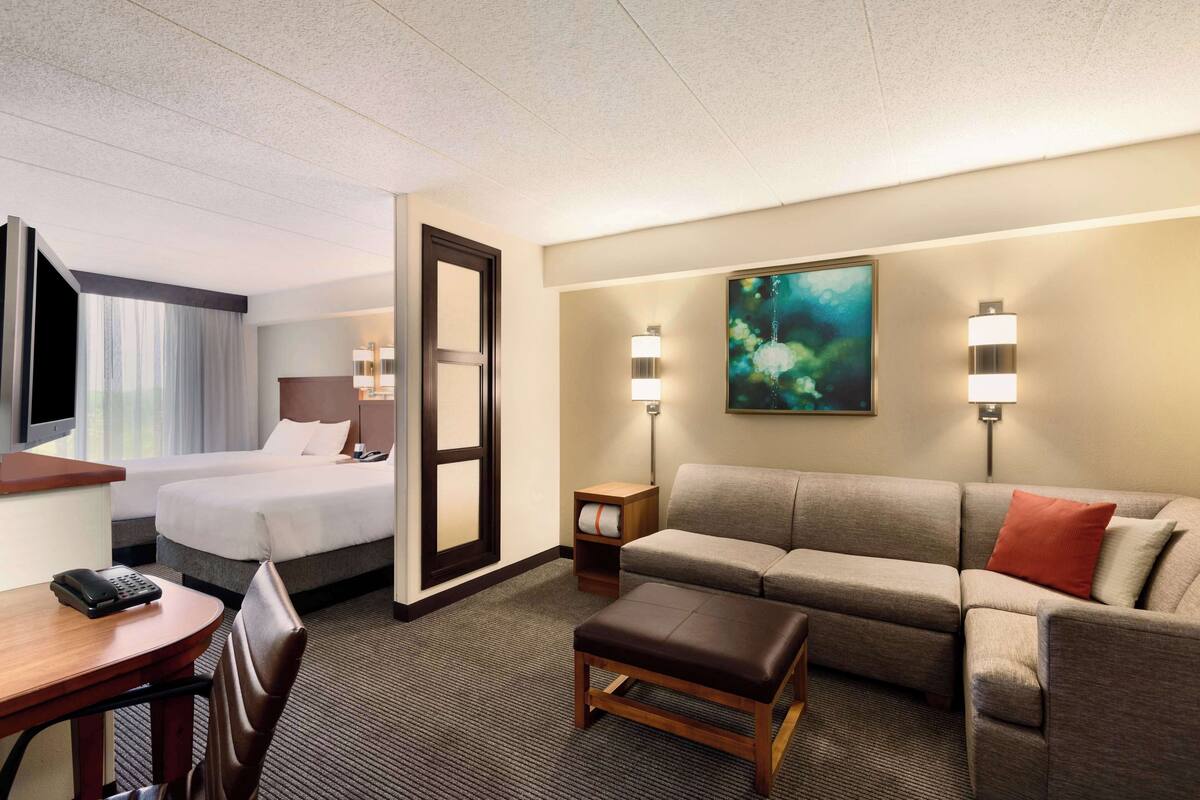 A hotel room with a bed, a sofa, a desk with a phone, and two wall-mounted lamps.
