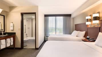 A hotel room with two beds, a bathroom, and a view of the outdoors.