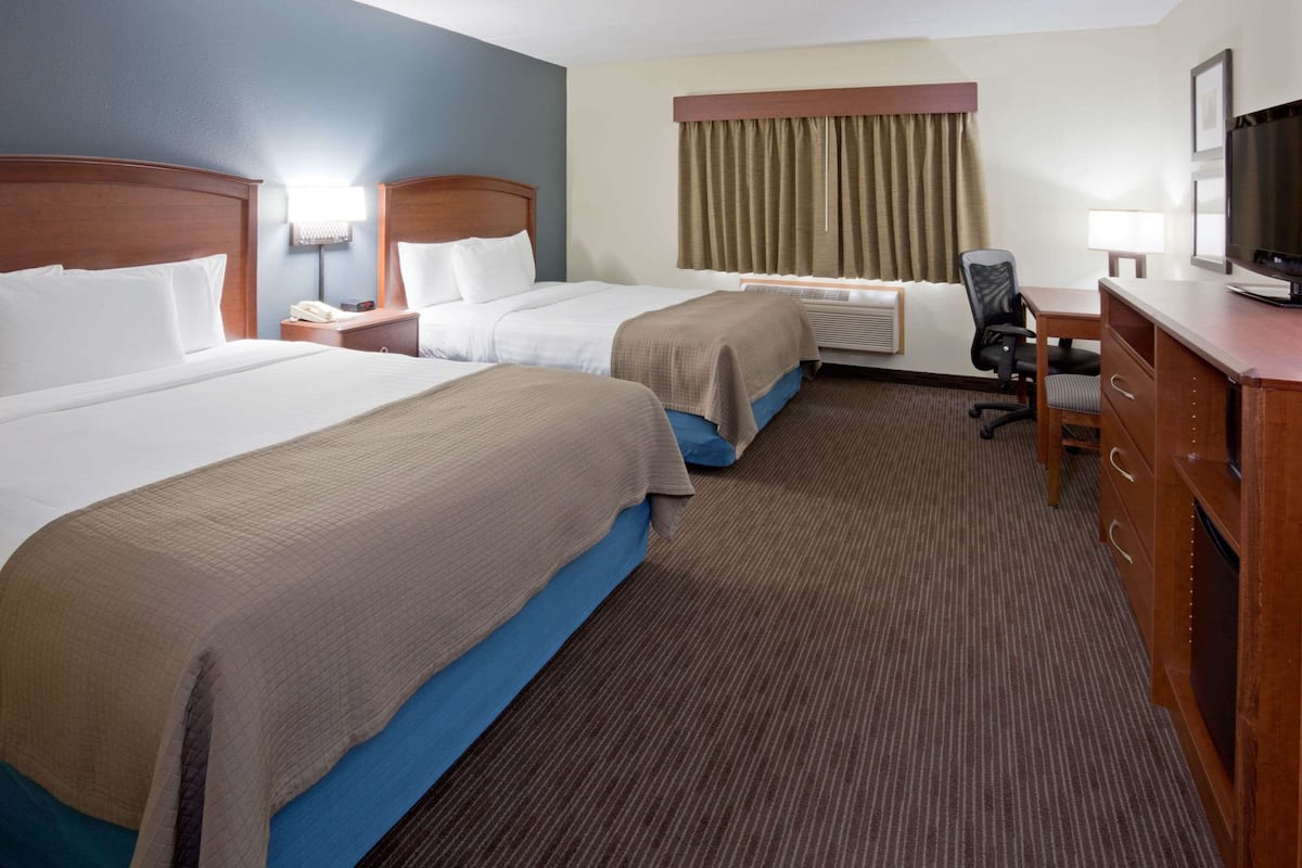 A hotel room with two beds, a desk, a chair, a television, and an air conditioning unit.