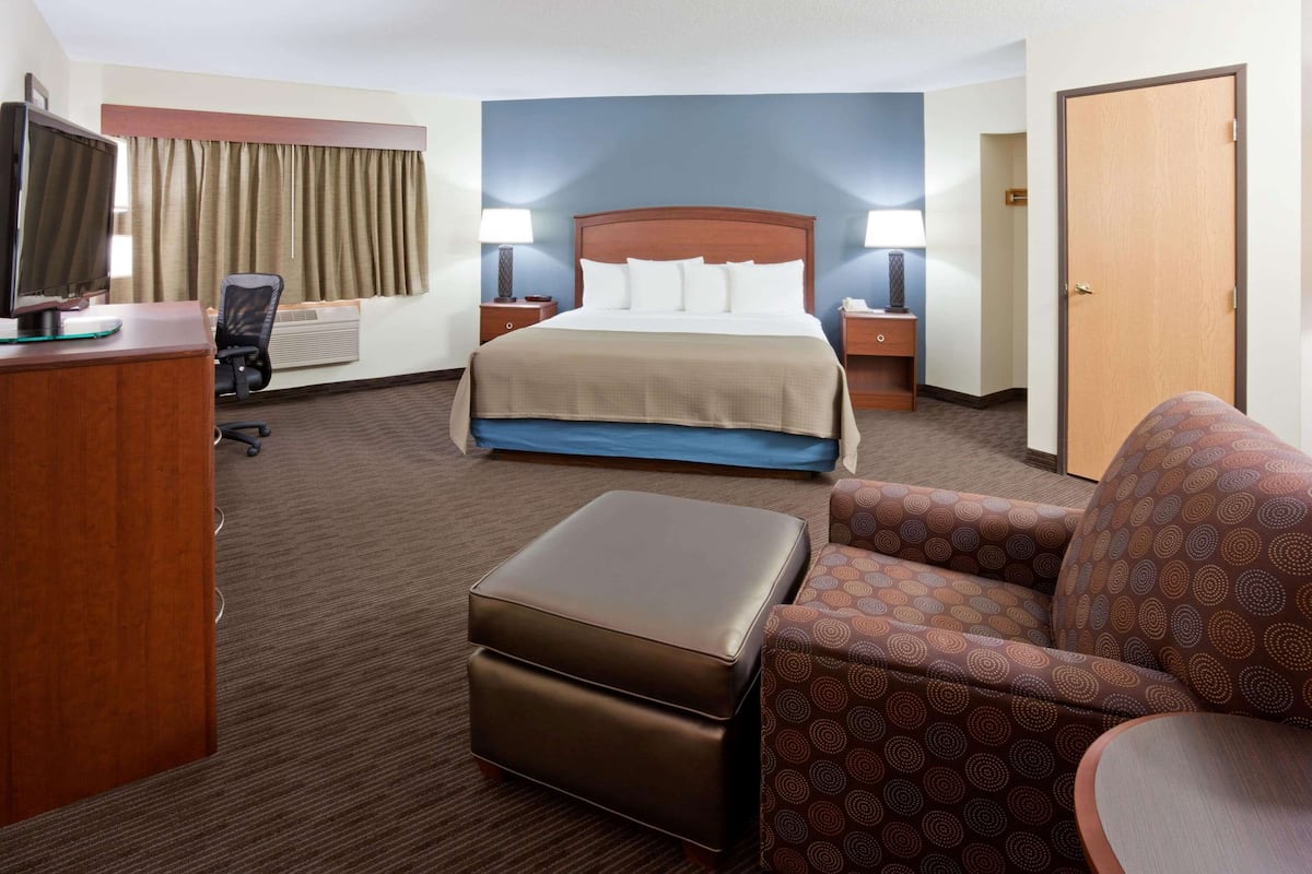 A hotel room with a bed, a desk with a computer, a chair, a sofa, and a door.
