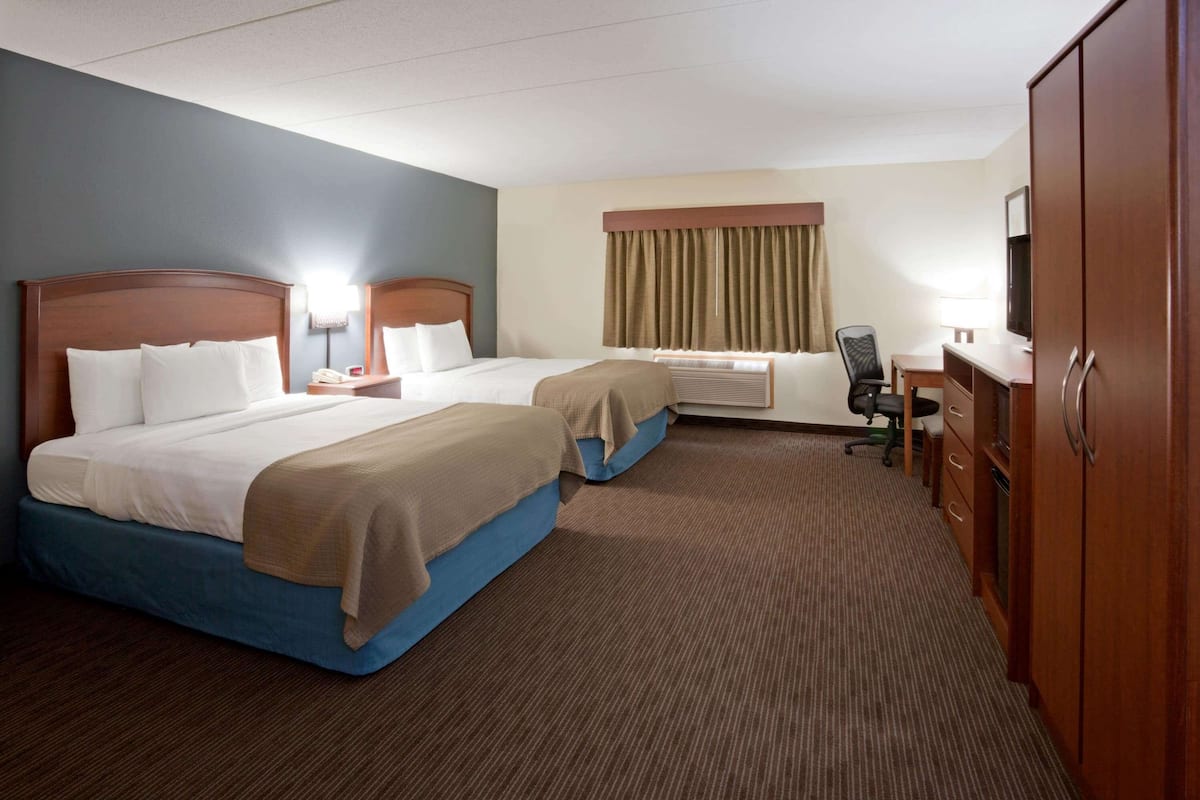 A hotel room with two beds, a desk, a chair, a TV, and a wardrobe.