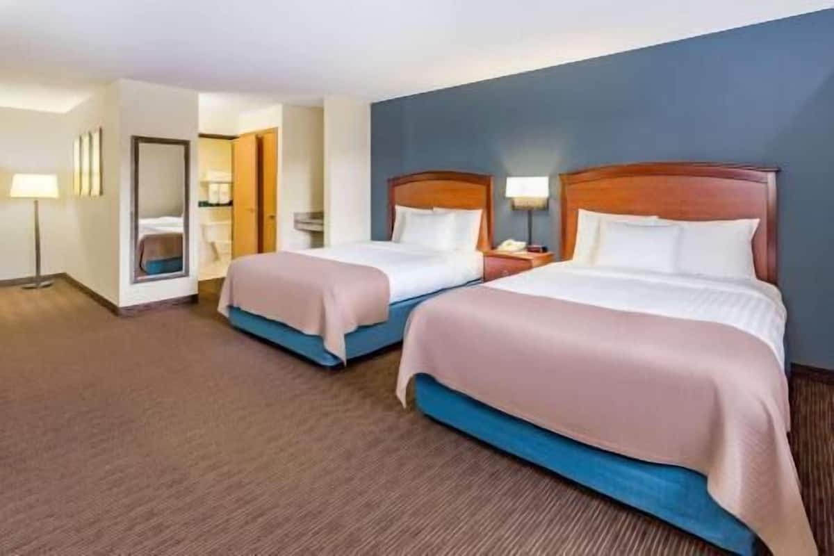Two beds with wooden headboards, a bedside table with a lamp, and a mirror on the wall.