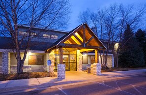 A building with a stone facade, a wooden entrance canopy, and a wheelchair-accessible entrance. - AmericInn by Wyndham Princeton MN (Princeton)